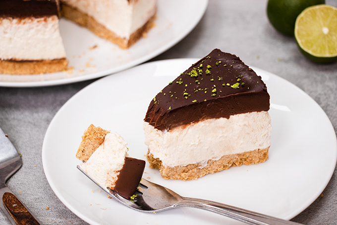 A slice of dairy free chocolate and lime cheesecake on a white plate with a forkful taken off the end.