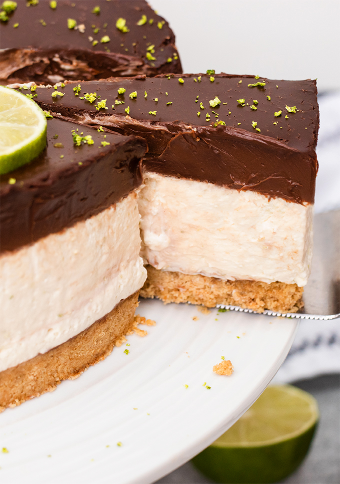 Close up of a slice being taken out of dairy free lime cheesecake with a chocolate ganache topping.