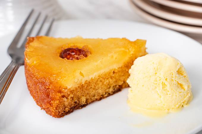 One slice of pineapple upside down cake on a white place with a scoop of vanilla ice cream next to it.