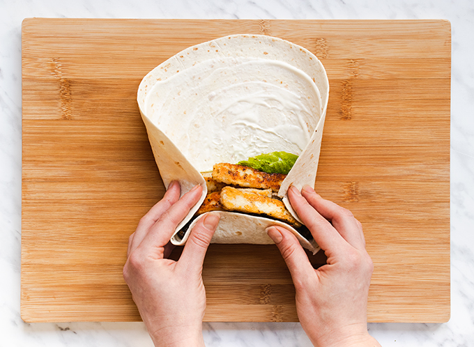 Top down view of a mushroom and halloumi wrap on a wooden board, being rolled up.