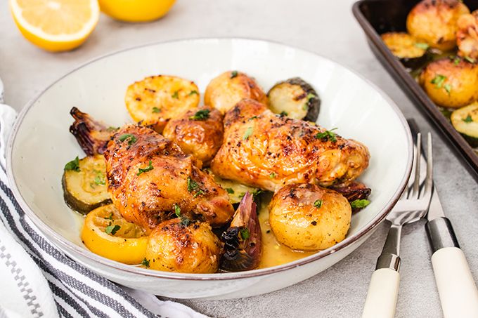Roast lemon and garlic chicken thighs in a bowl with vegetables and potatoes.