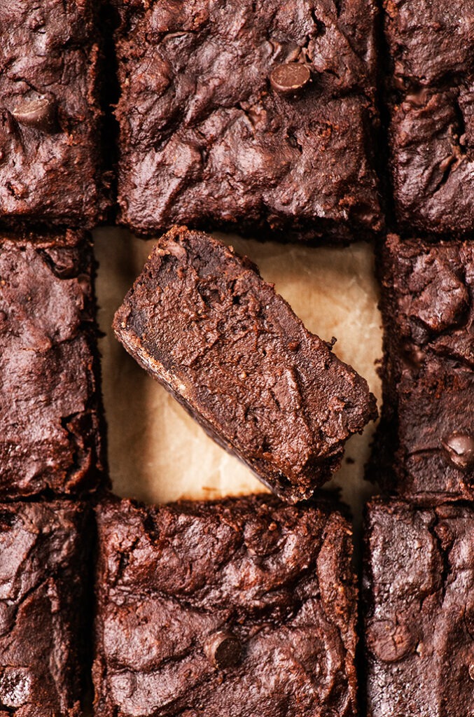 Close up of a fudgy vegan chocolate brownie turned on its side, surrounded by other brownies.