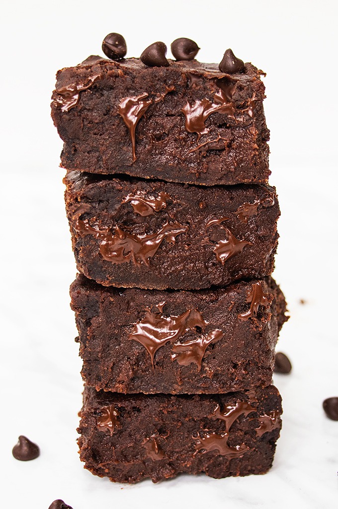 A stack of four gooey vegan date brownies with chocolate chips scattered around.