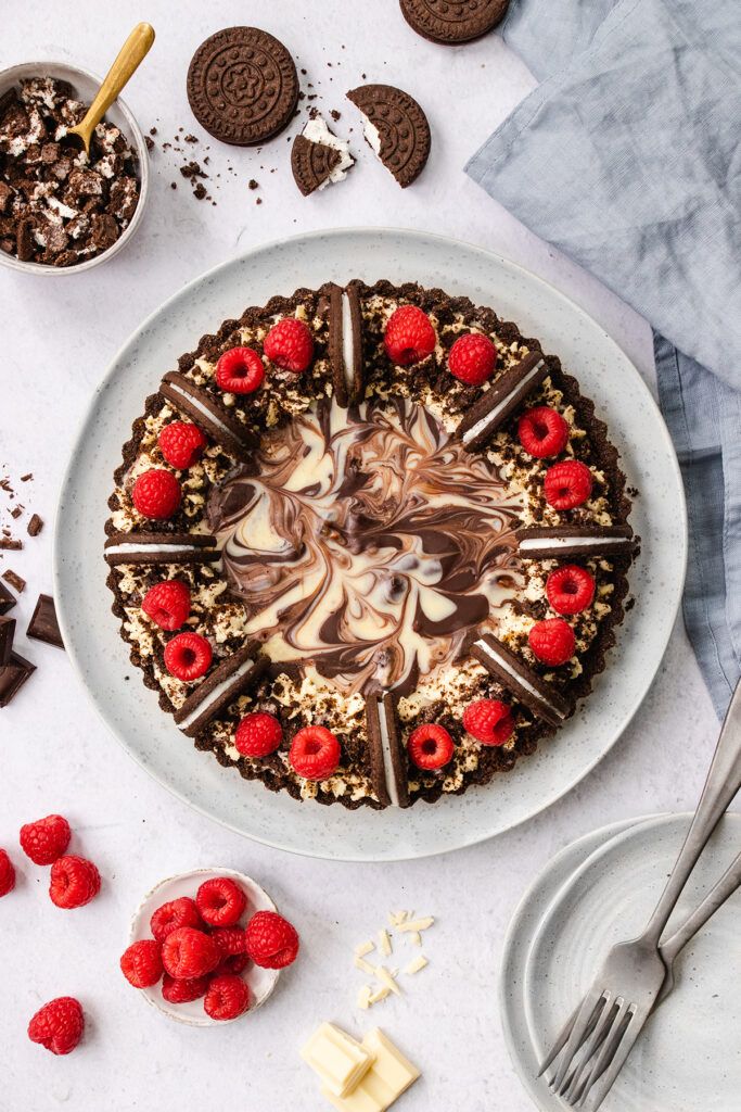 Top down view of a chocolate marble tart, decorated with raspberries and cookies and cream biscuits.