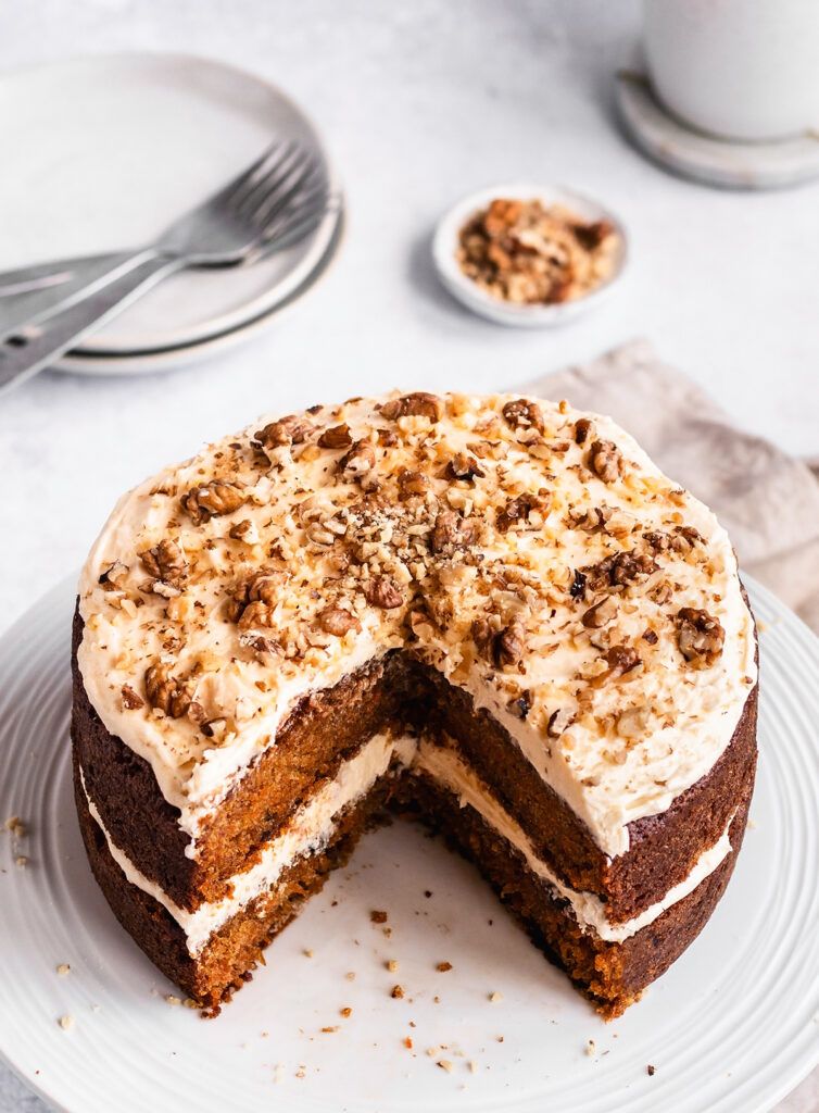 A carrot cake with frosting, topped with chopped walnuts.