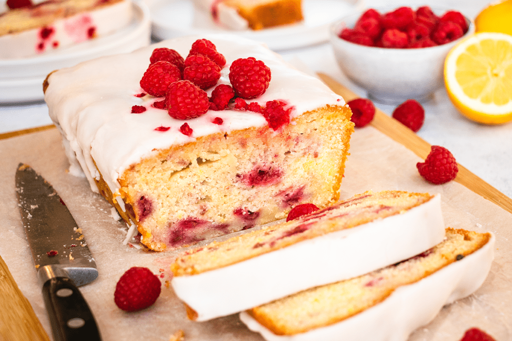 A lemon and raspberry drizzle cake, cut into slices on a board.