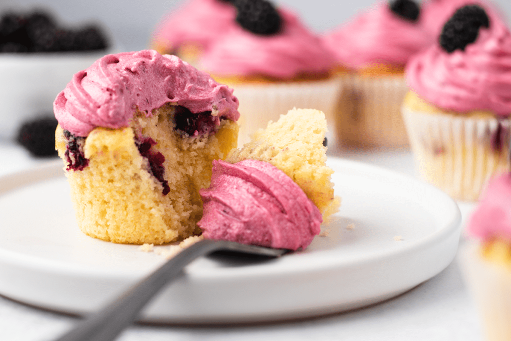 A blackberry cupcake on a plate with a forkful cut away to reveal berries in the centre of the cake