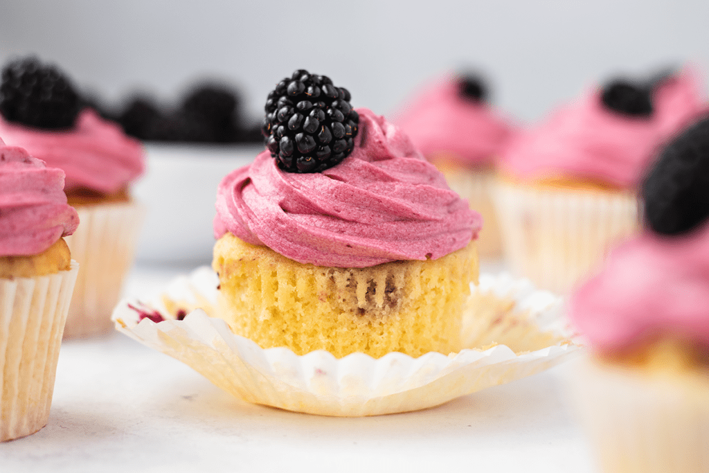A blackberry cupcake with the cupcake case peeled away from the sides to reveal the vanilla sponge cake