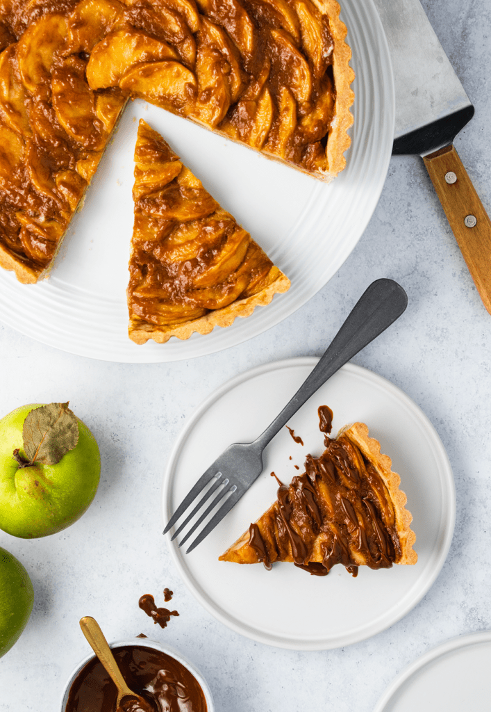 Top down view of a toffee apple tart with one slice on a plate