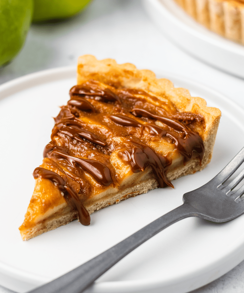 A slice of toffee apple tart on a plate with dulce de leche drizzled over it