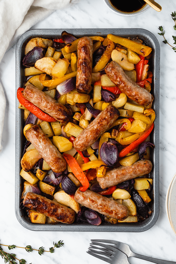 Top down view of baked sausages and vegetables on a tray
