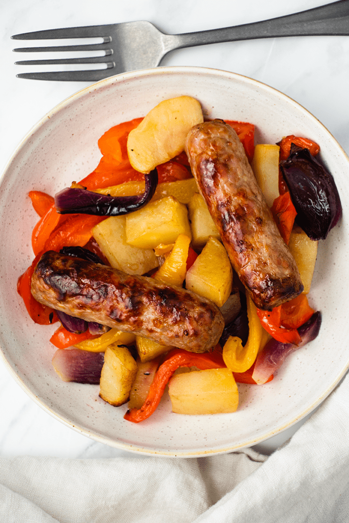 Close up top down view of roasted sausages and vegetables in a dish