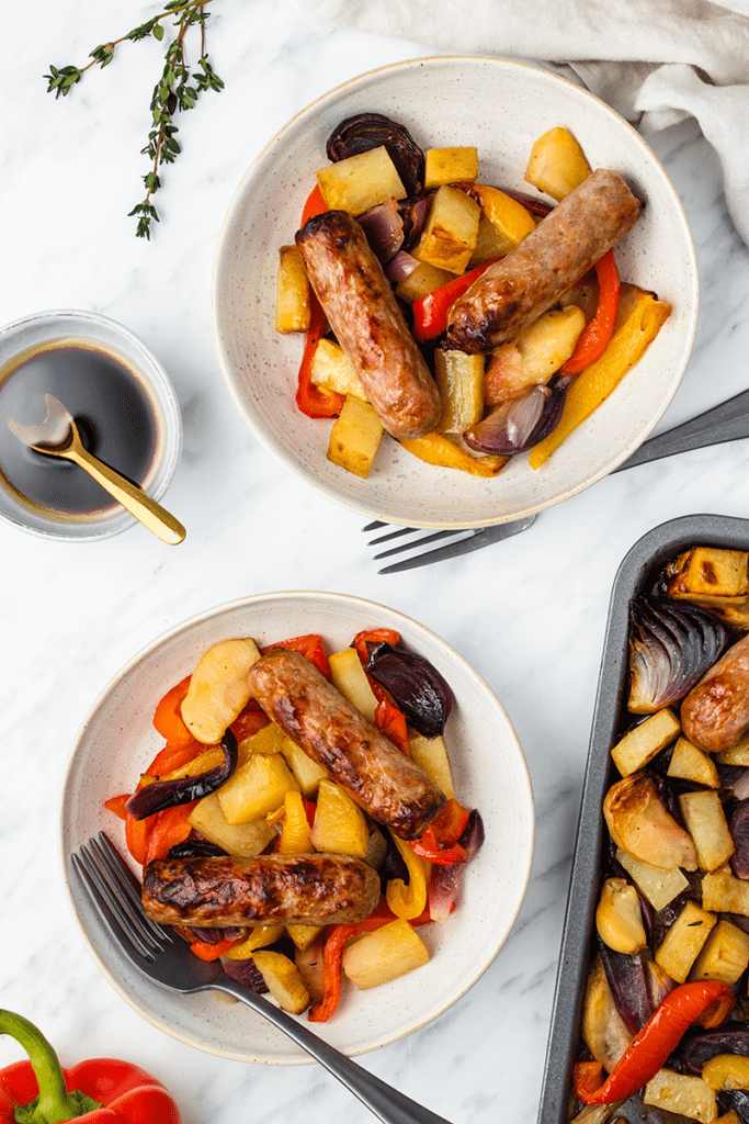 Top down view of two dishes of a roasted sausage and vegetable dinner