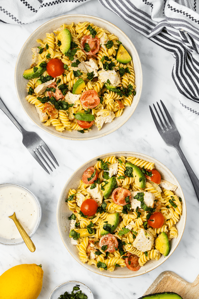 Top down view of two bowls of chicken avocado pasta salad