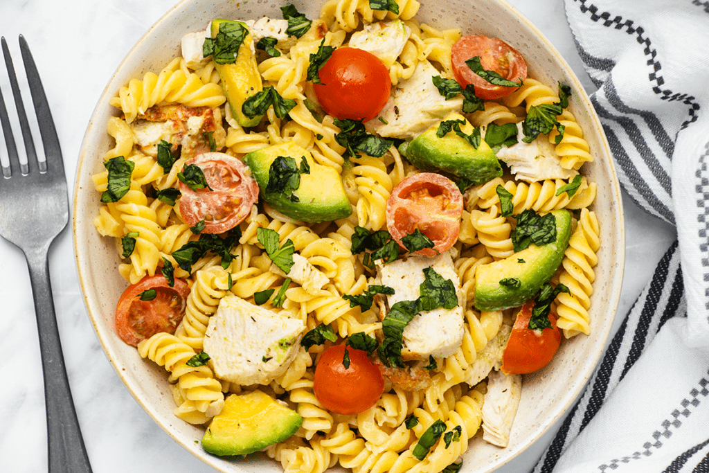 A bowl of pasta salad with chicken, avocado and tomatoes