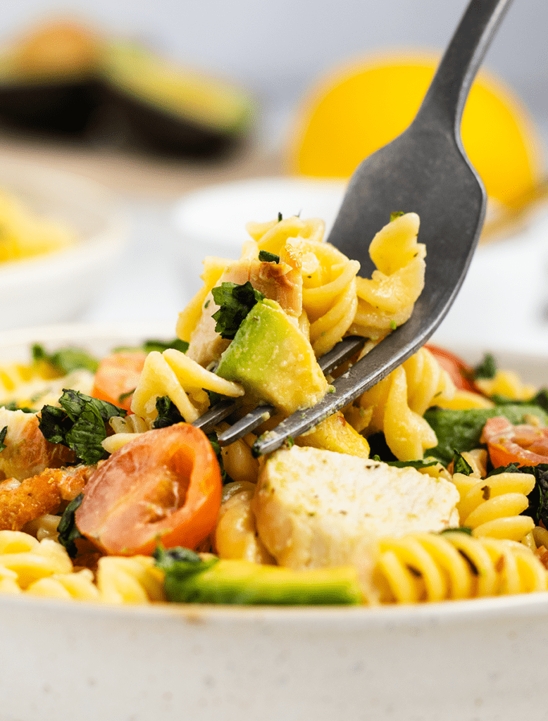 Close up of a fork digging into a bowl of chicken pasta salad