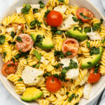 A bowl of pasta salad with chicken, avocado and tomatoes